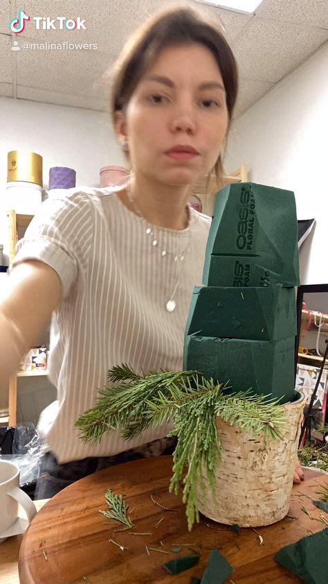 a woman is making an origami house out of wood and greenery on a table