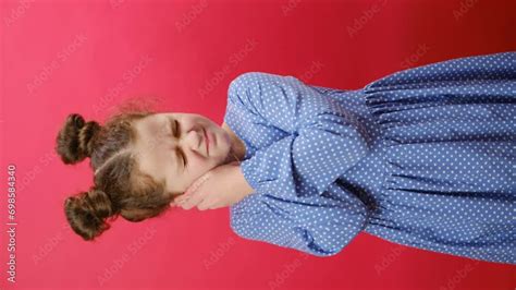 Vertical footage of unhappy little girl child suffering from ear pain, posing isolated over red ...