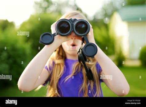 Funny little girl looking through binoculars on sunny summer day. Child exploring distant views ...