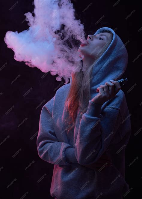 Premium Photo | Portrait of beautiful blonde girl in gray hoodie smokes vape isolated on black ...