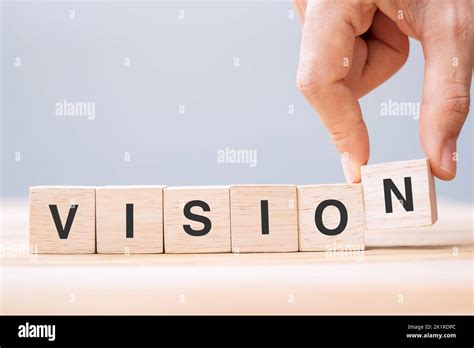 Business man hand holding wooden cube block with VISION business word on table background ...