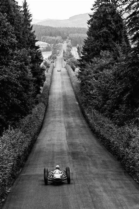 black and white photograph of a race car going down a road with trees on both sides