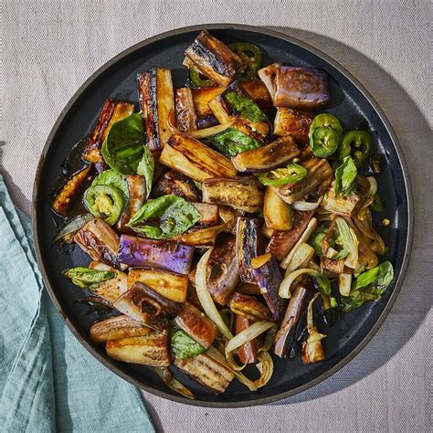 a pan filled with vegetables and meat on top of a table next to a blue towel