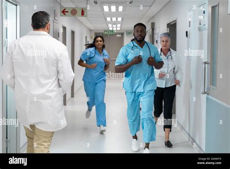 Diverse group of male and female doctors running through busy hospital ...