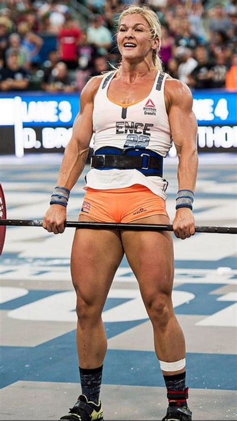 a woman in orange shorts and white shirt holding a barbell while standing on top of a