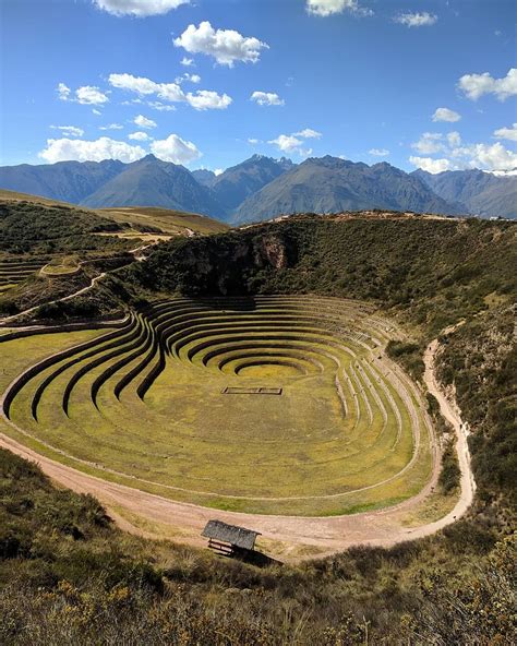 an aerial view of a large circular structure in the middle of a grassy field with mountains in ...