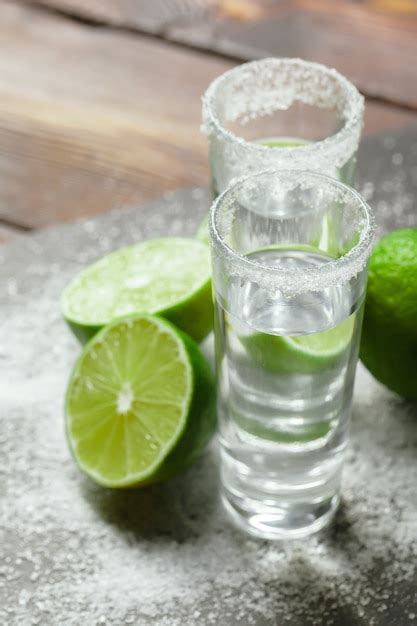 Premium Photo | Tequila silver shots with lime slices and salt on wooden board