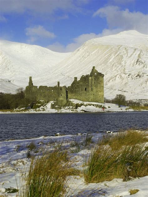 an old castle sitting on top of a snow covered hill next to a body of water