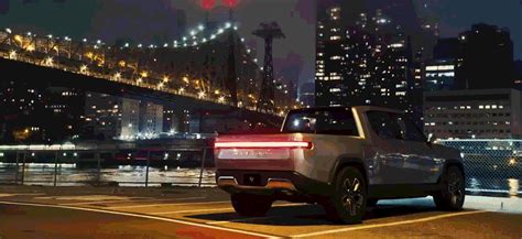 the rear end of a silver suv driving down a street in front of a bridge at night