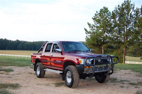 a red pick up truck parked on top of a dirt road next to a field