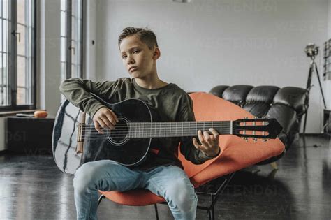 Boy playing guitar while sitting on chair at home stock photo