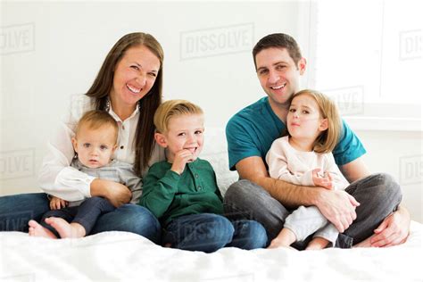 Portrait of family with three children (2-3, 4-5) sitting on bed - Stock Photo - Dissolve