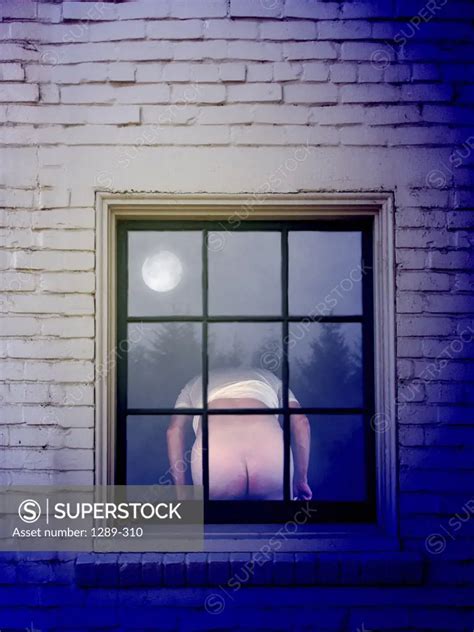 Rear view of a man mooning in the window of a house - SuperStock