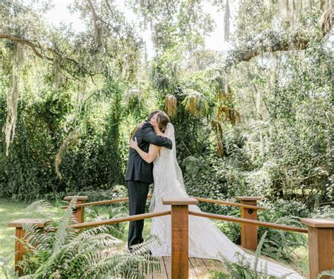 a bride and groom kissing on a bridge in the woods at their outdoor ...