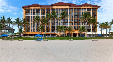 a hotel on the beach with palm trees and blue umbrellas in front of it