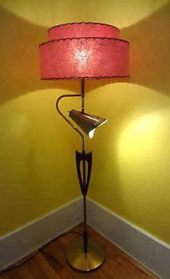 a floor lamp with a pink shade on it in a corner next to a yellow wall
