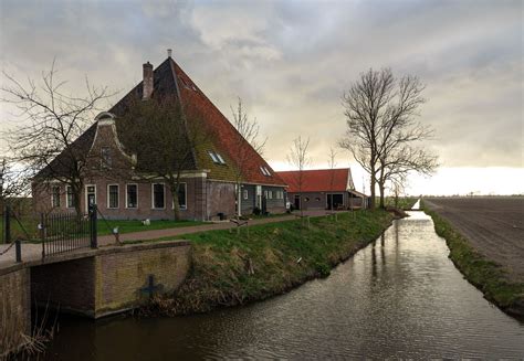 an old house on the side of a river next to a small bridge and farm