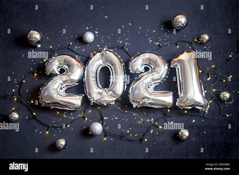 Silver foil balloons made numbers 2021 on black background with garland. Holiday party ...