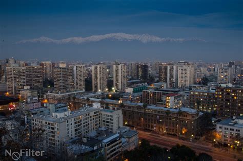 the city is lit up at night with snow capped mountains in the backgroud