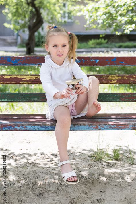 Beautiful little girl sitting on an old bench shakes the sand out of the flip-flops Stock Photo ...