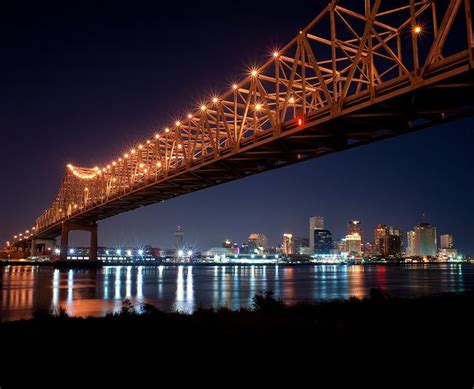 a bridge that is over some water with lights on it and buildings in the ...