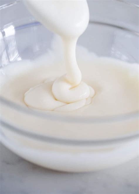 a glass bowl filled with white liquid and a whisk being poured into it