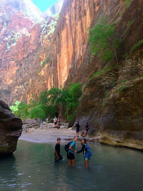 several people are wading through the water in front of a mountain side cliff face