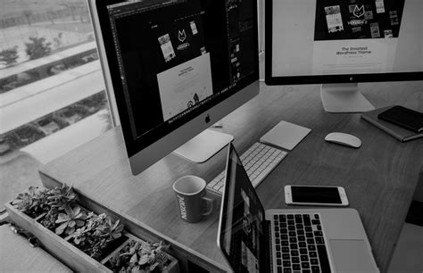 two computer monitors sitting next to each other on top of a wooden desk in front of a window