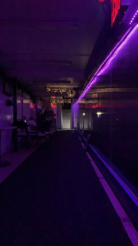 an empty hallway with purple lights and benches
