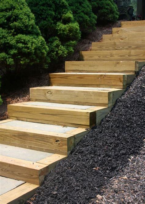 wooden steps leading up to the top of a hill in front of trees and bushes