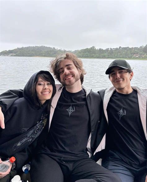 two men and a woman sitting on a boat in front of the water with their arms around each other