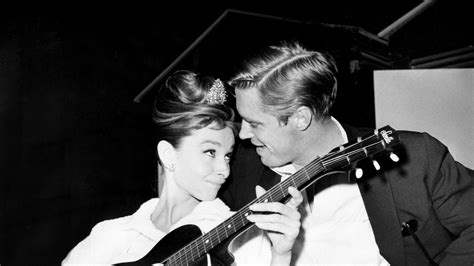 Audrey Hepburn strums a guitar for her costar George Peppard between takes on the set of ...