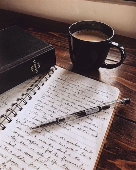 an open notebook and pen sitting on top of a wooden table next to a cup ...