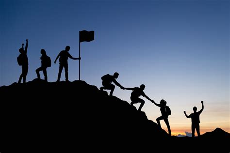 Silhouette of people helping each other hike up a mountain at sunset background. Teamwork ...