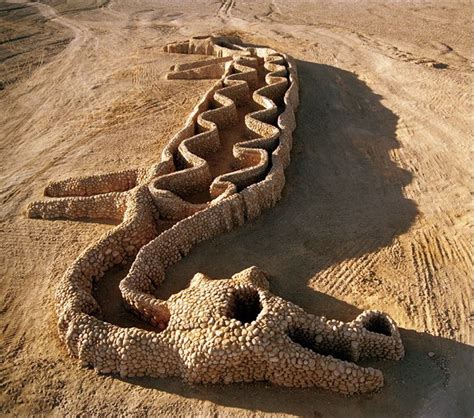 an animal made out of sand sitting on top of a dirt field