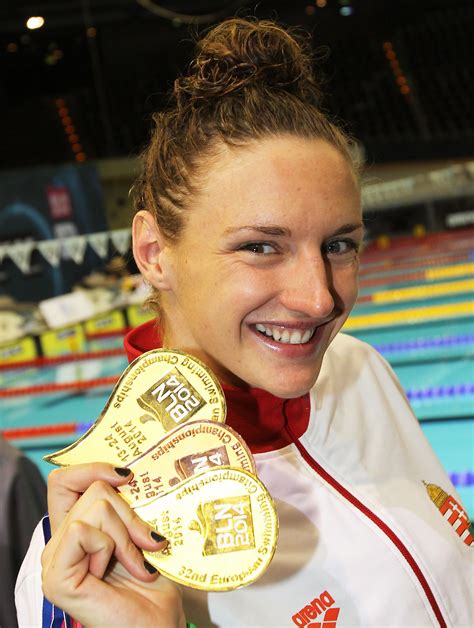 a woman holding up a gold medal in front of a swimming pool