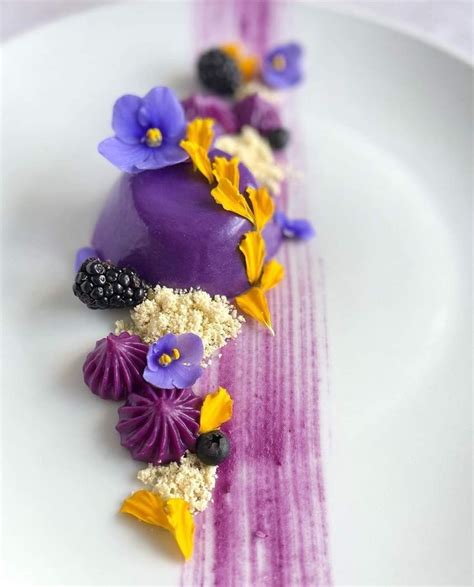 a white plate topped with purple cake covered in flowers and berries on top of it