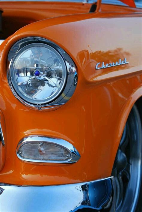 the front end of an orange classic car with chrome rims and headlamps