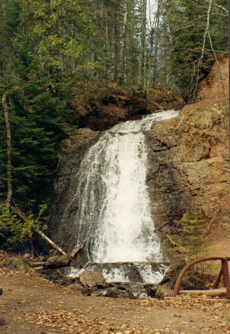 a man sitting on a bench in front of a waterfall with trees around him ...