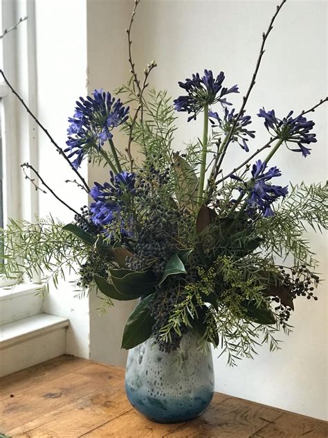 a vase filled with blue flowers sitting on top of a wooden table next to a window