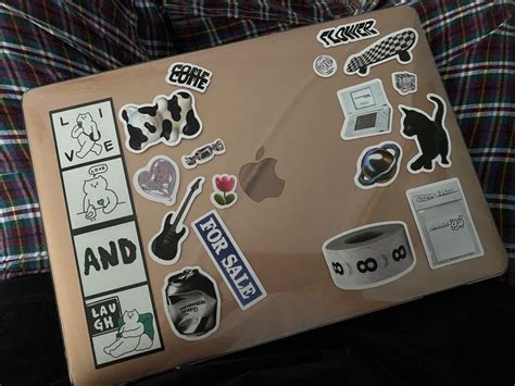 an open laptop computer covered in stickers and decals on a plaid cloth ...