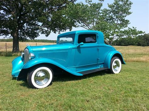 an old blue truck is parked on the grass in front of a tree and fence