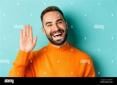 Close-up of friendly young man smiling, waving hand to say hello ...