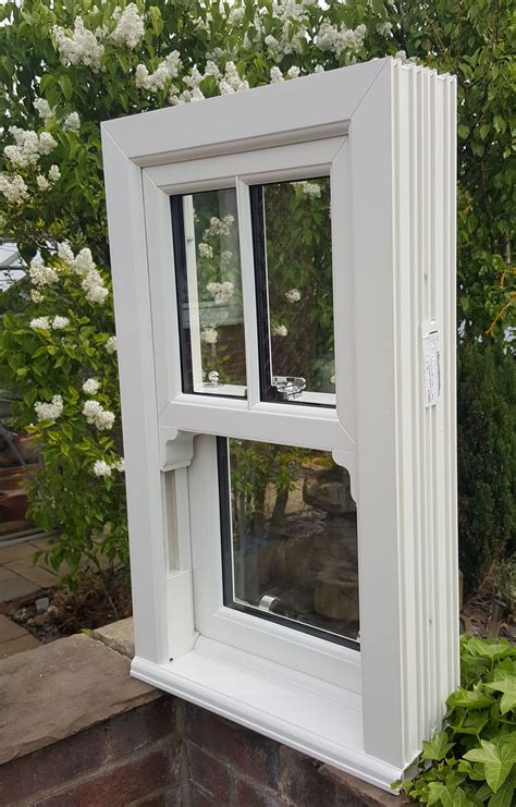 a white window sitting on top of a brick wall next to a lush green bush