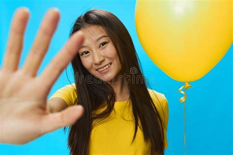 Asian Woman Holding a Yellow Balloon on a Blue Background in a Yellow T-shirt Smiling with Teeth ...