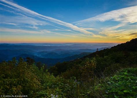 the sun is setting in the mountains with trees and bushes on either ...