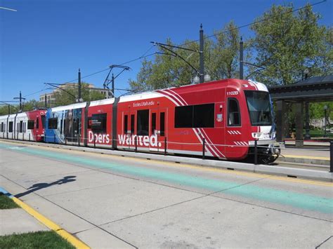 a red and white train traveling down tracks next to a sidewalk on a sunny day