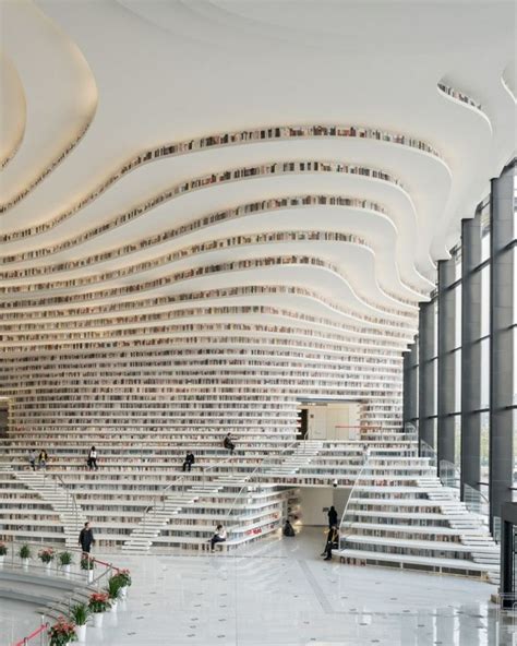 the interior of a large building with lots of bookshelves and people walking around