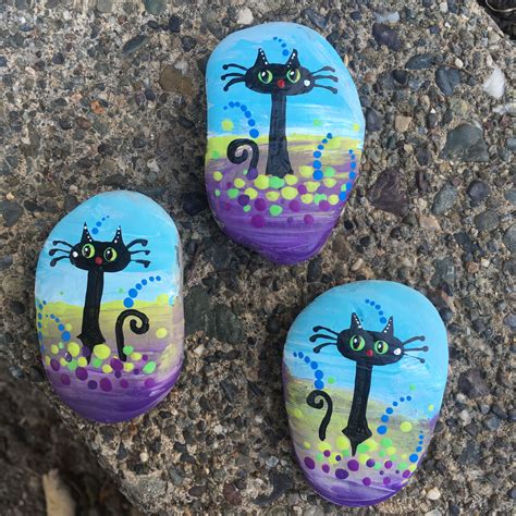 three painted rocks with black cats on them