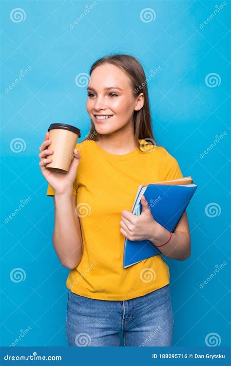 Young Woman Smiles and Holds Books and a Glass of Coffee or Tea in Her Hands on a Blue ...